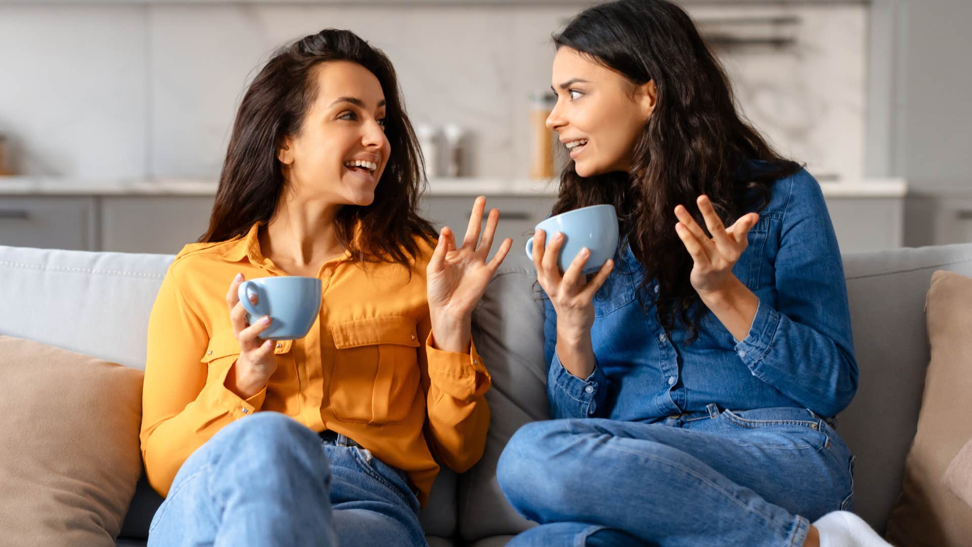 Two women gossiping together on a couch.