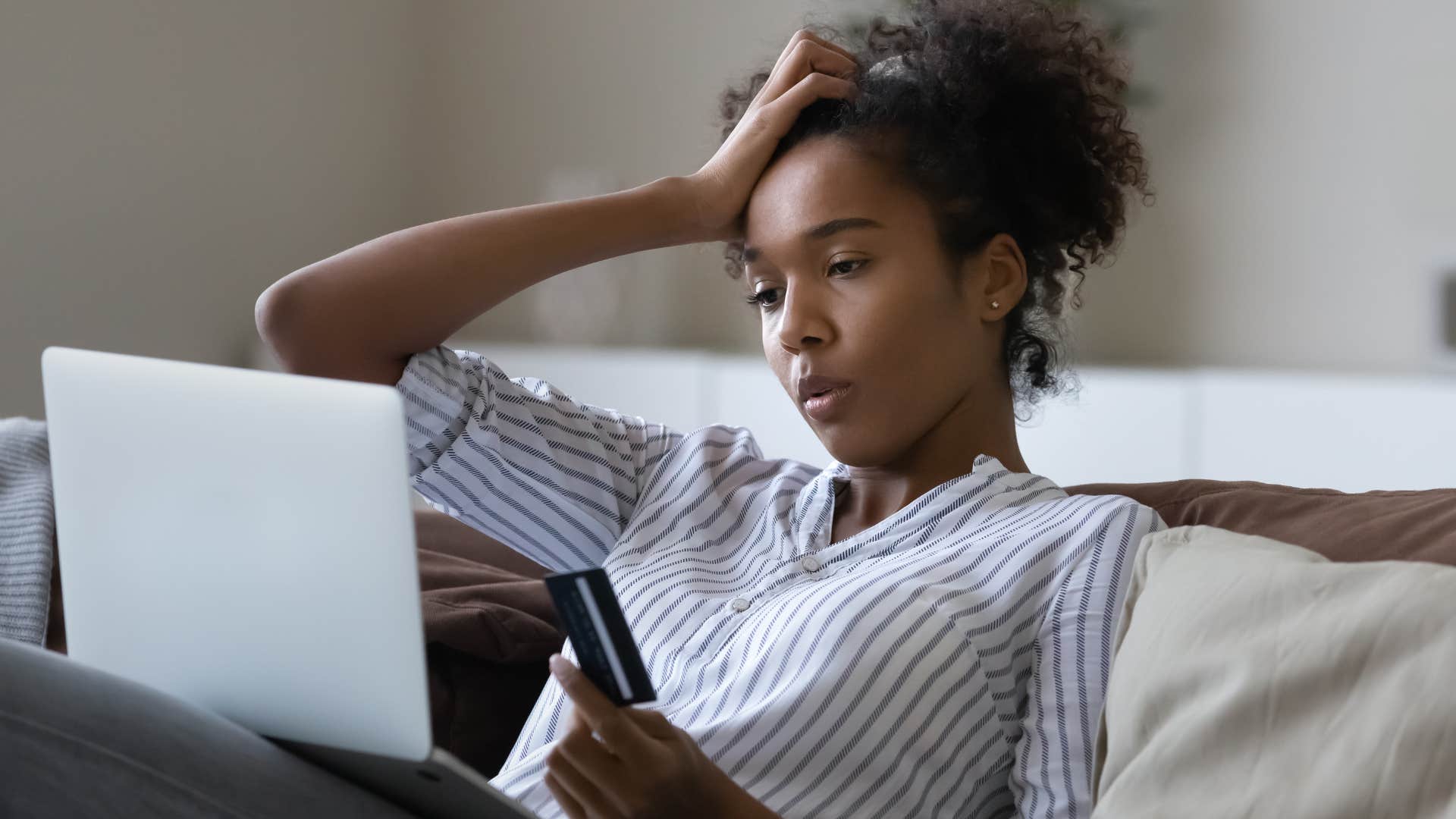 Woman holding her head looking stressed on the couch.