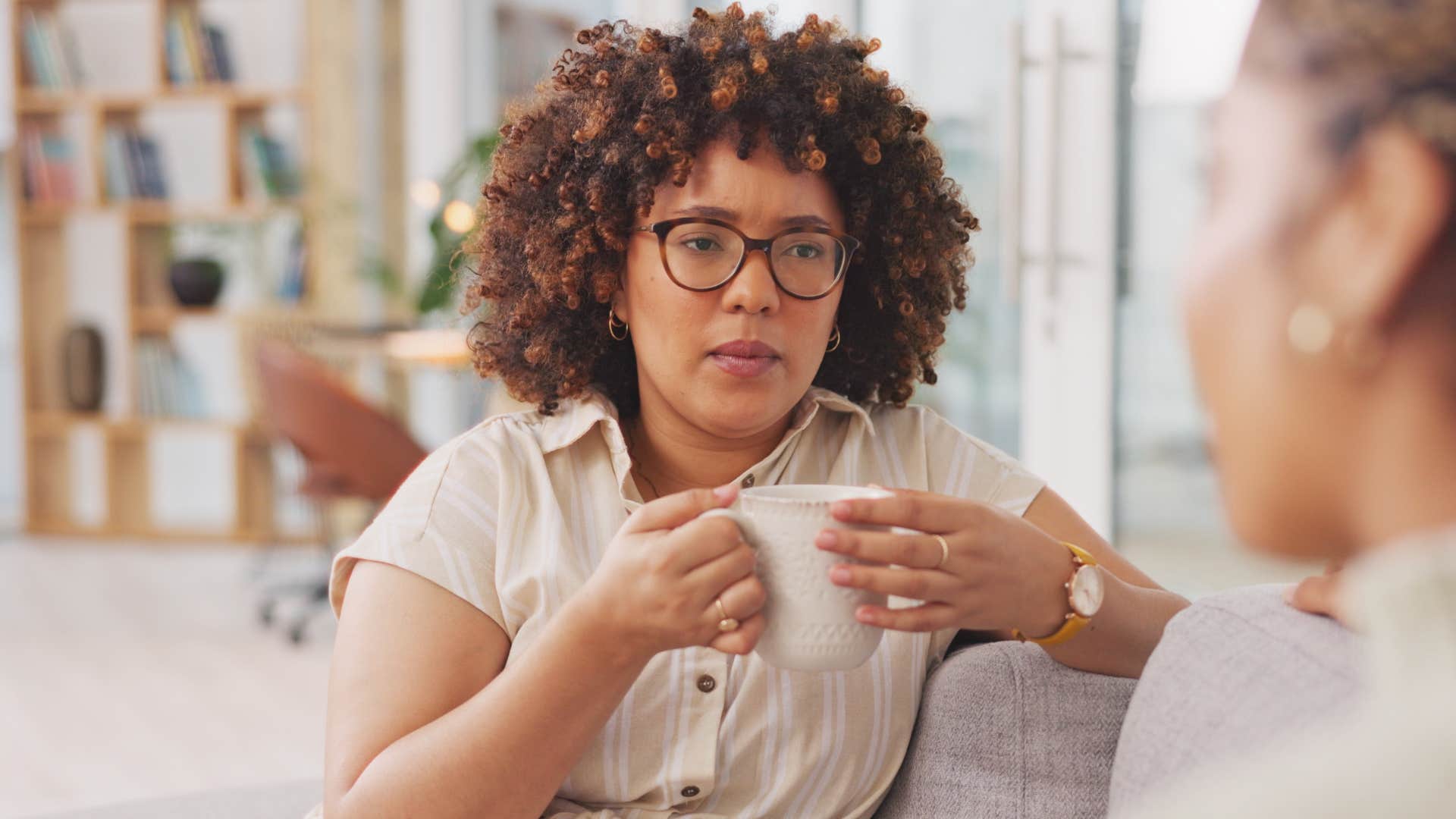 Woman holding a coffee mug and looking seriously at her friend.