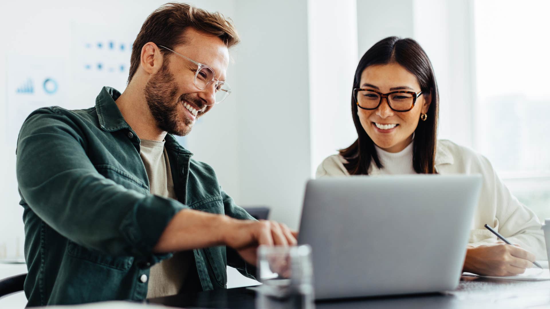 Co-workers smiling and talking together at a desk.