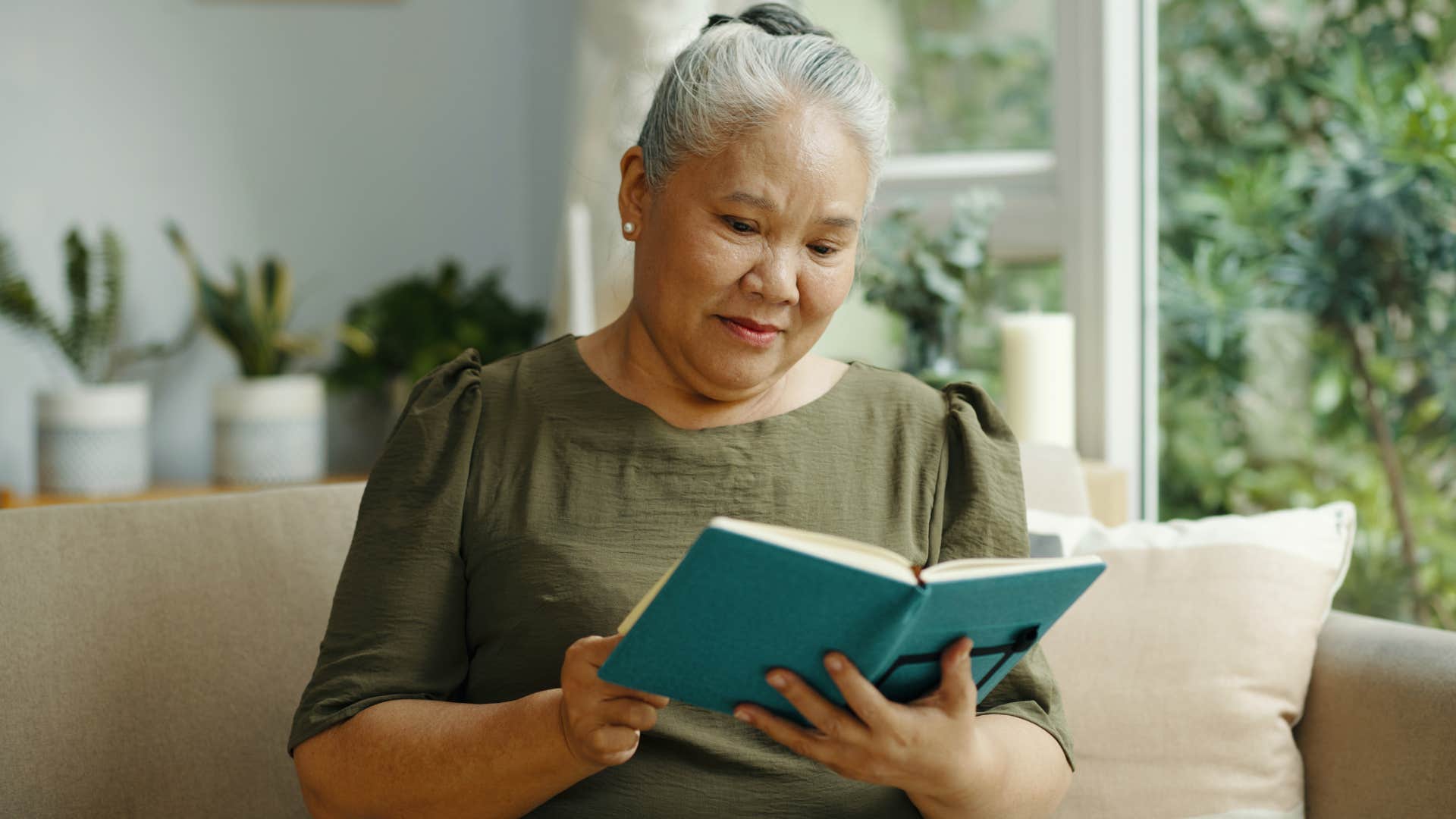 Older woman reading a book on a couch.