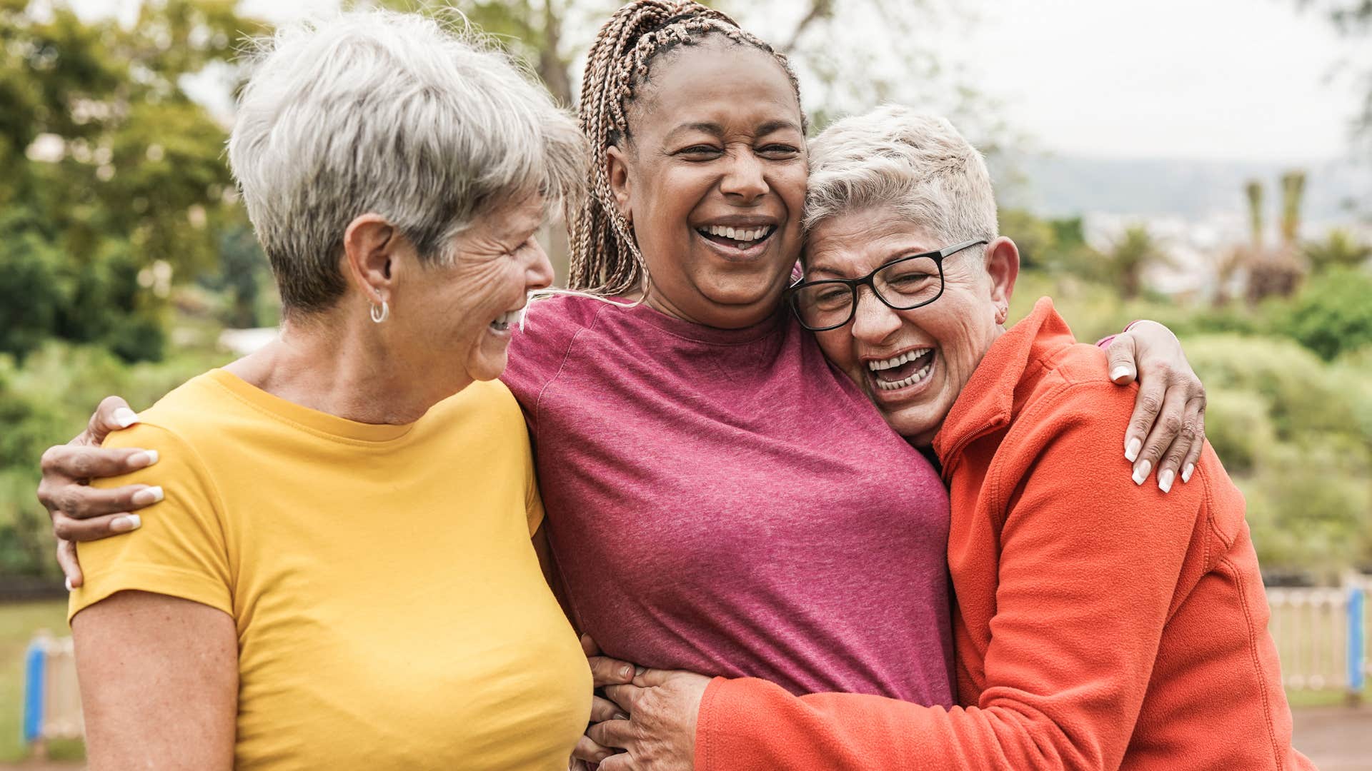 Three older women smiling and hugging each other.