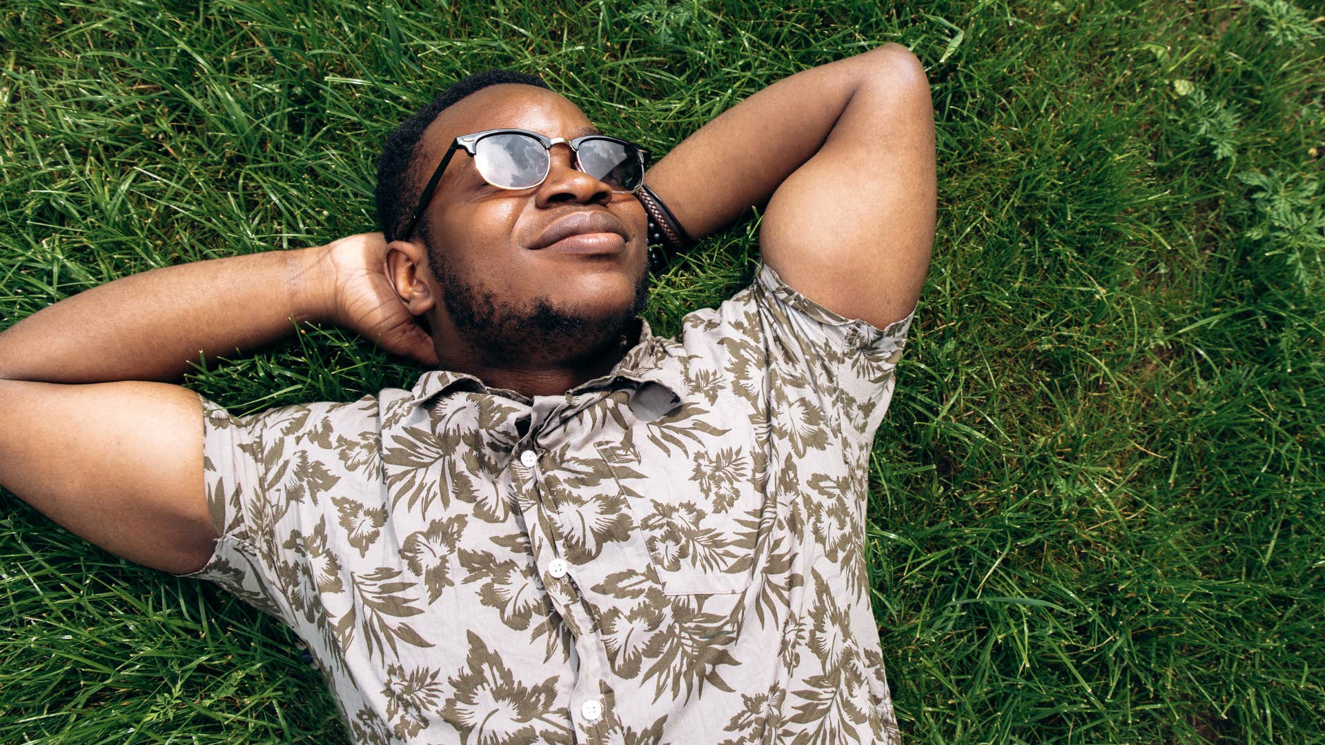 Man smiling and laying on the grass outside.