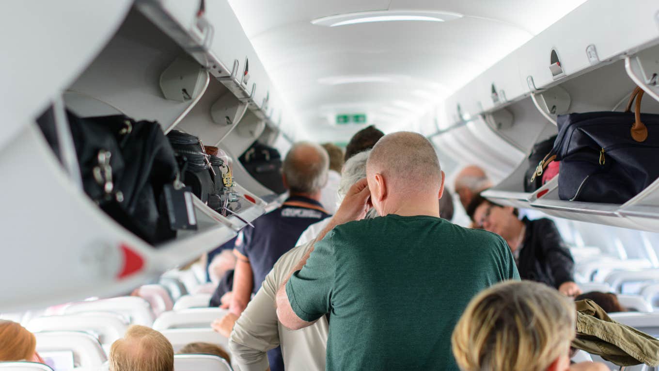 airline passengers standing and sitting while waiting to deplane