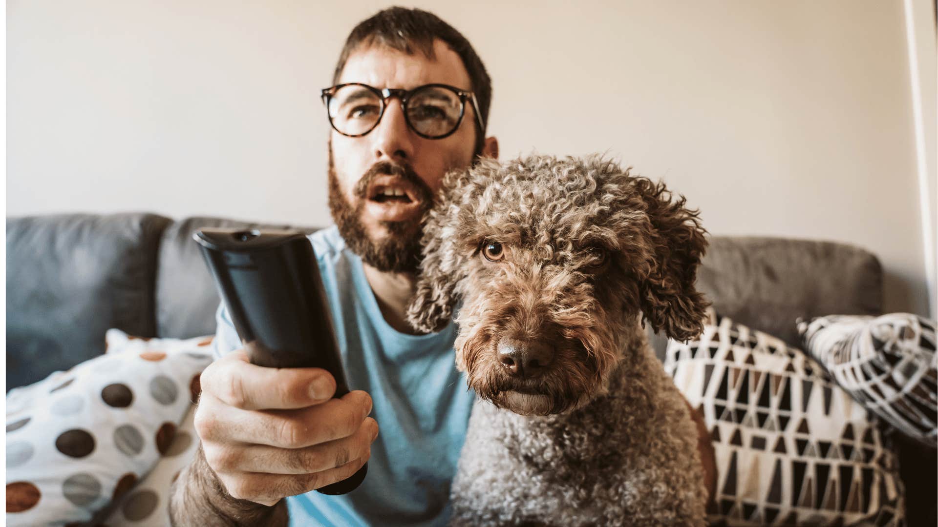 Perplexed man on couch with remote control on dog