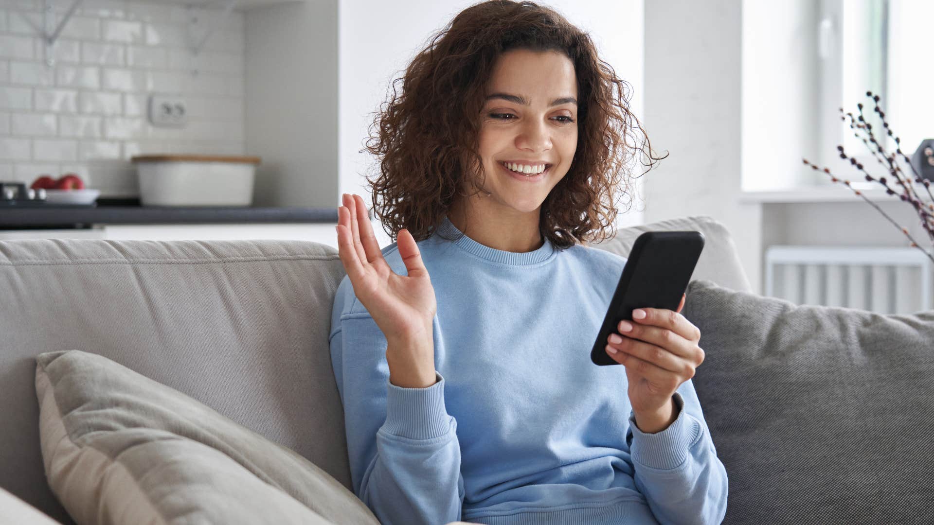 Young woman smiling and waving at her phone.