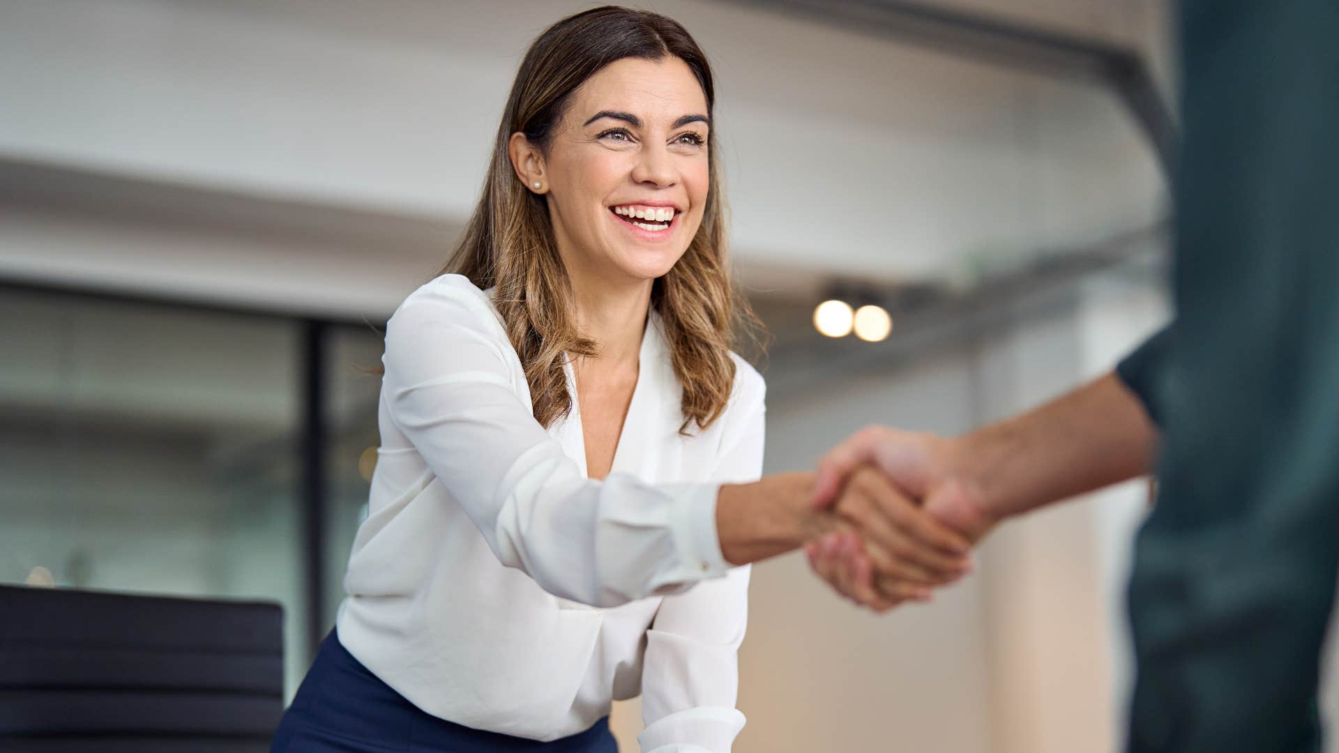 Woman smiling and shaking someone's hand.