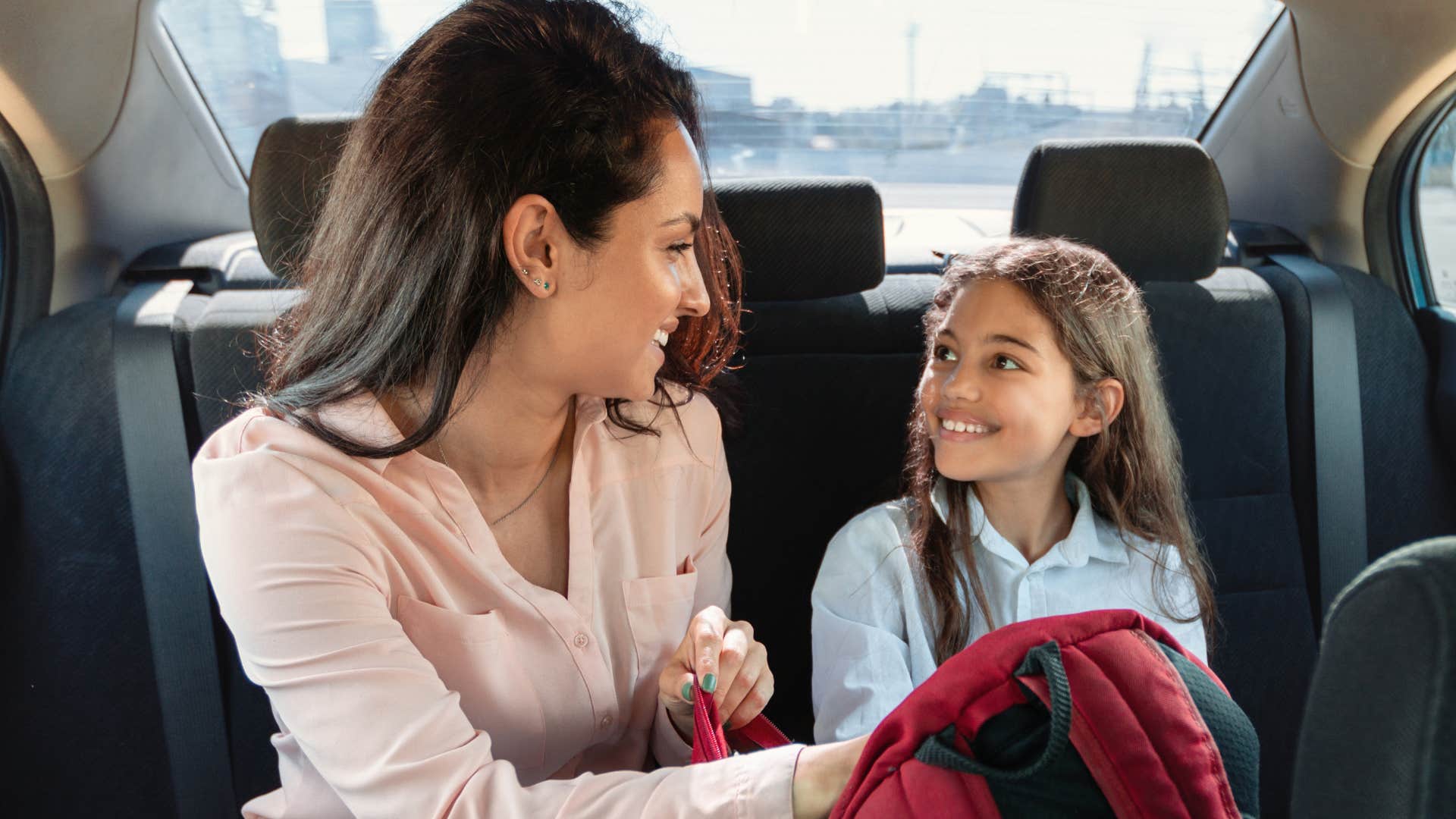 Woman smiling the backseat of a car with her young daughter