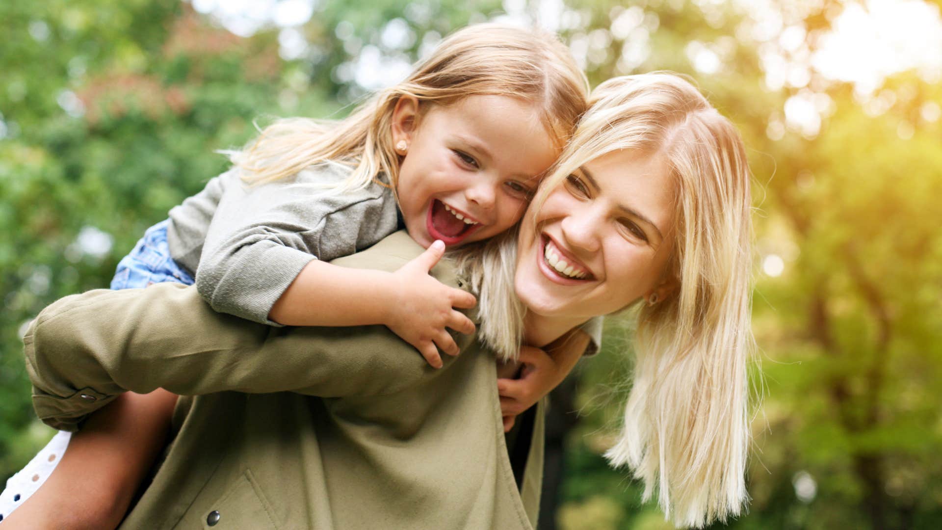 Woman smiling and holding her young daughter on her back