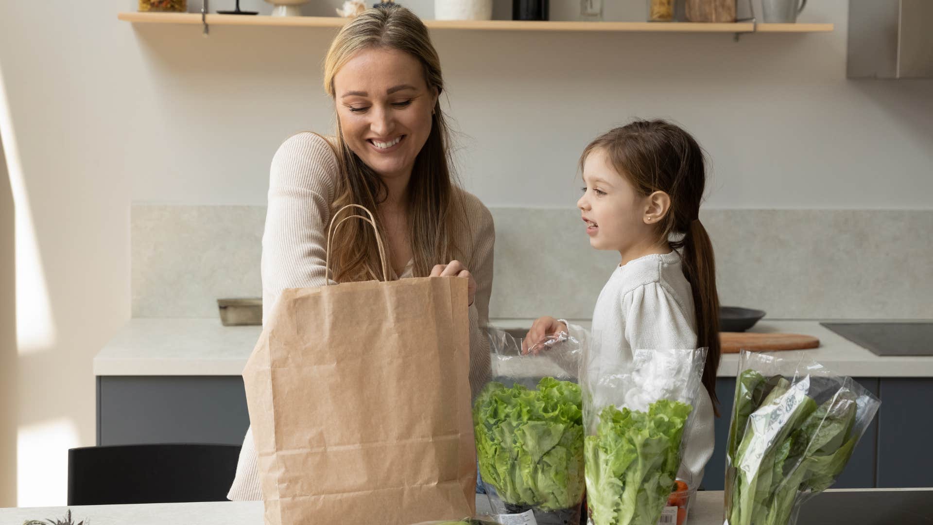 Woman unpacking groceries in her kitchen next to her daughter