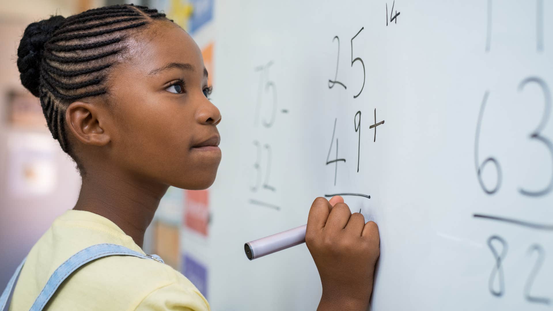 Young girl doing math problems on a white board