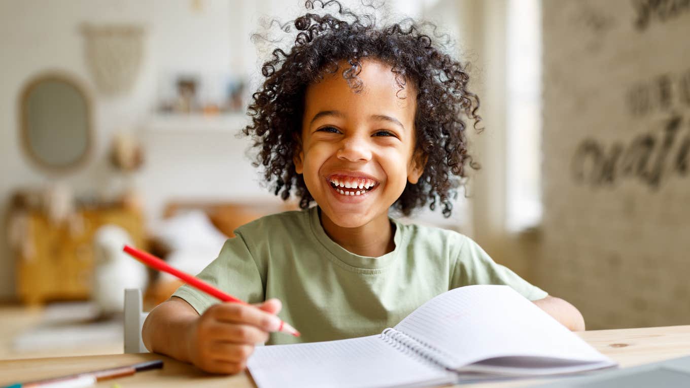 Little boy smiling and doing homework at a table.