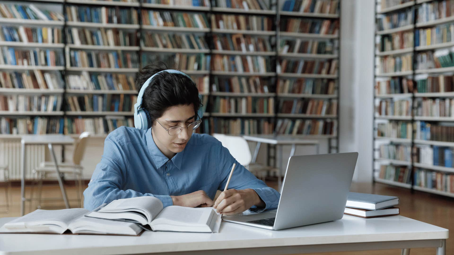 Person in library wearing headphones works on laptop