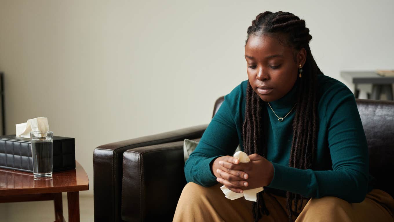 upset woman sitting on couch with tissue in hand