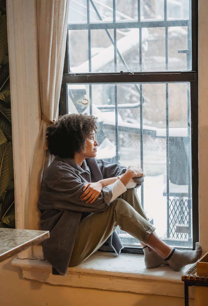 Woman looking out window feeling sad