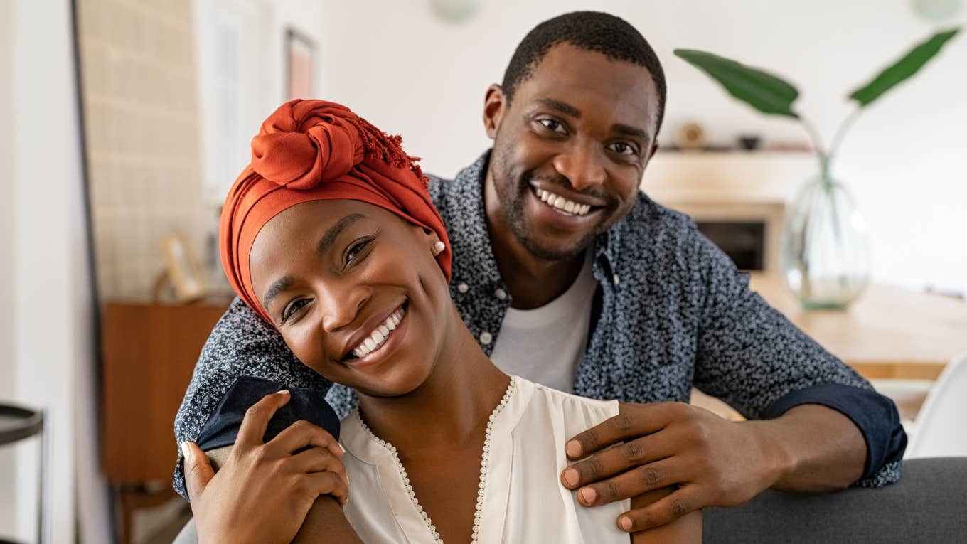 Portrait of adult happy african american couple hugging at home while sitting on couch.