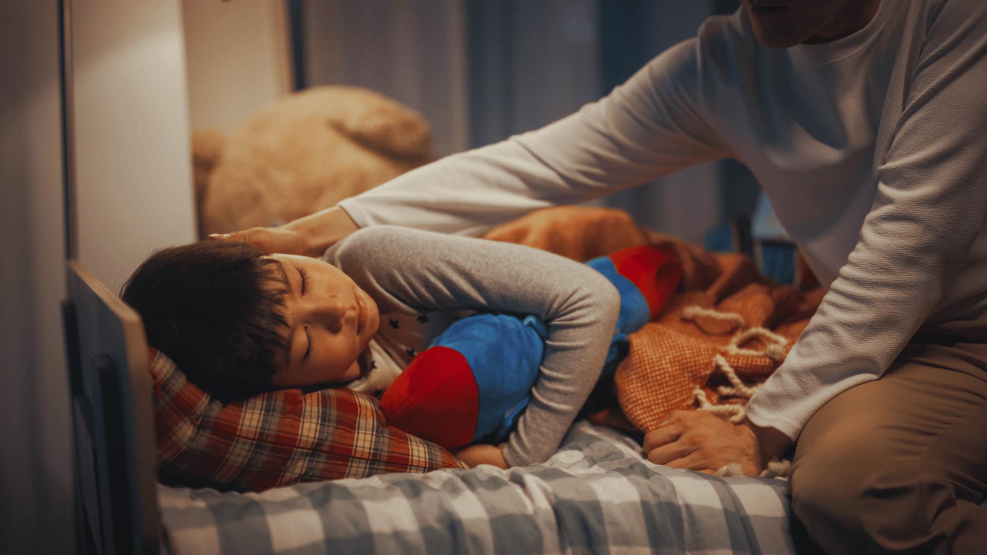 Parent tucks child into bed