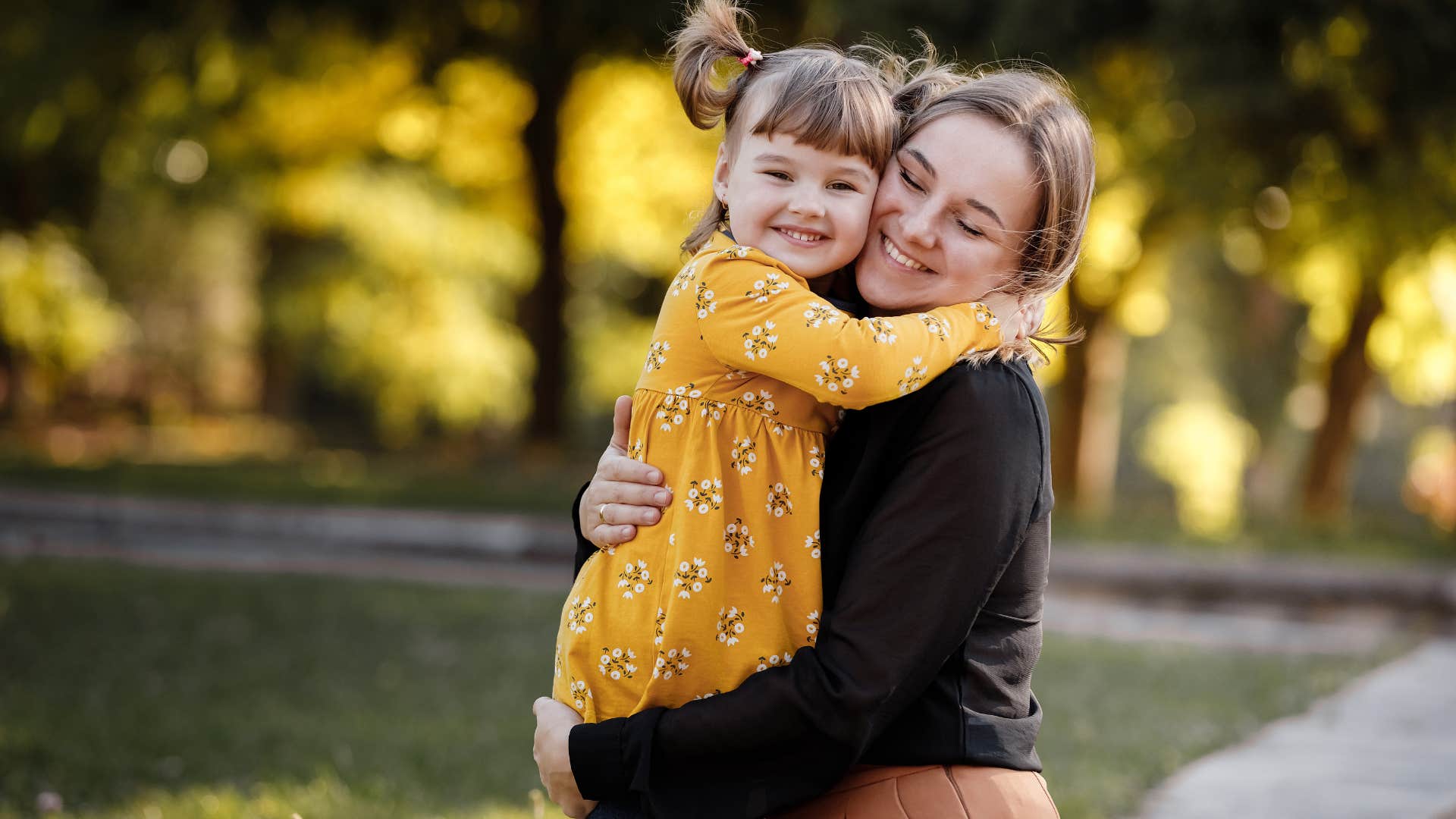 Woman hugging her young daughter outside.