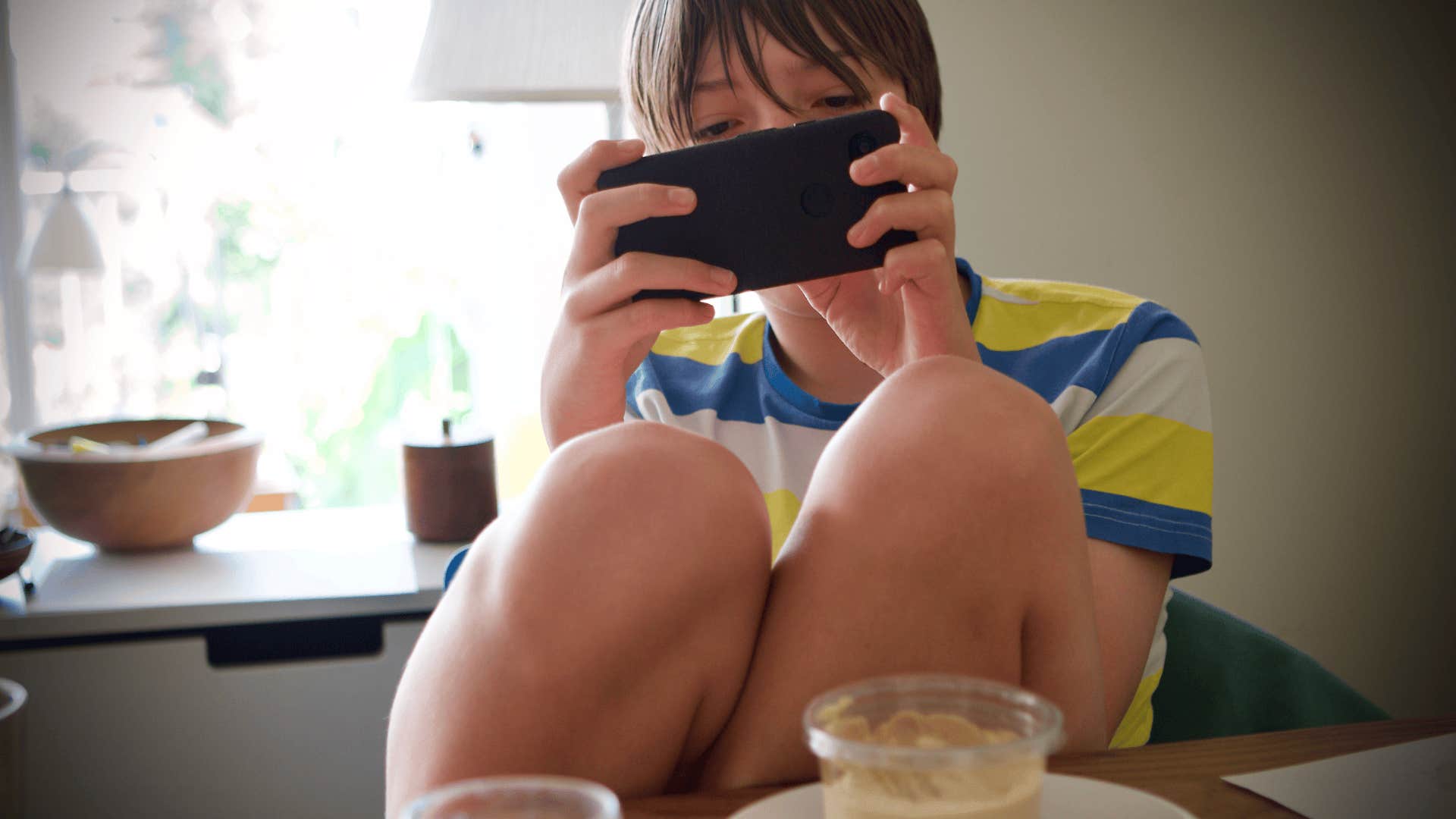  teenager with bad table manners using smartphone with knees up