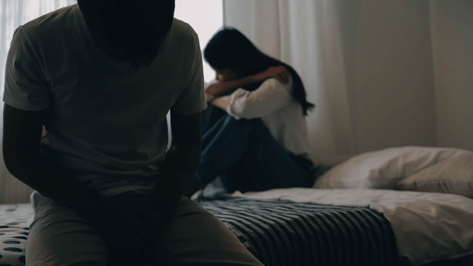 upset woman sitting on bed ignoring man