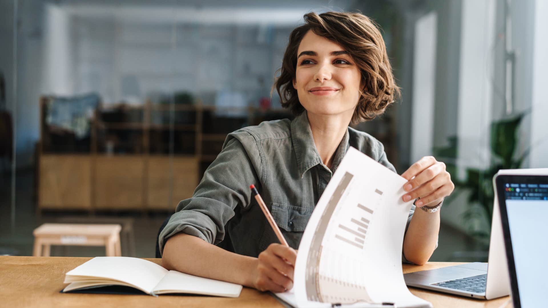 smiling woman writing down notes while sitting at table in office