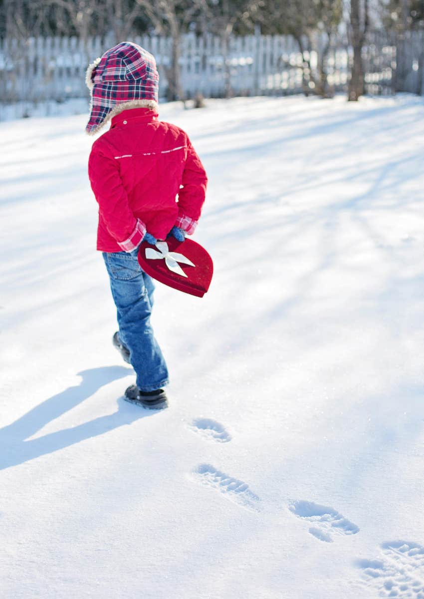 child carrying Valentine's Day gift from parent in the snow