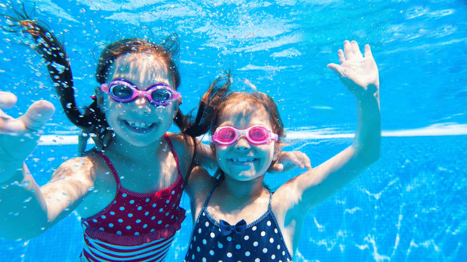 Two child underwater in swimming pool wave and smle