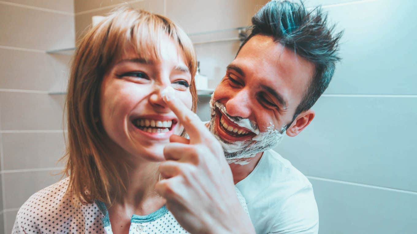 Young married couple having fun playing with shaving foam in the bathroom