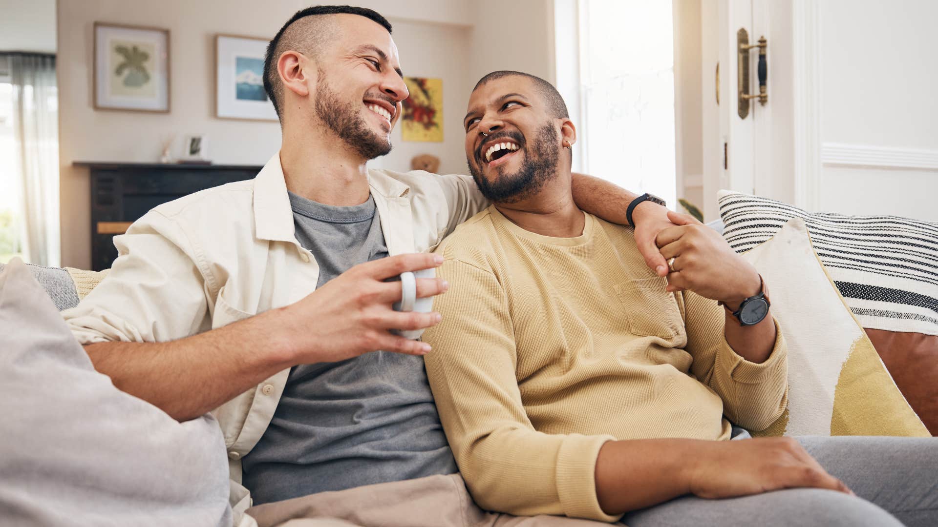 Gay couple smiling and talking on a couch.