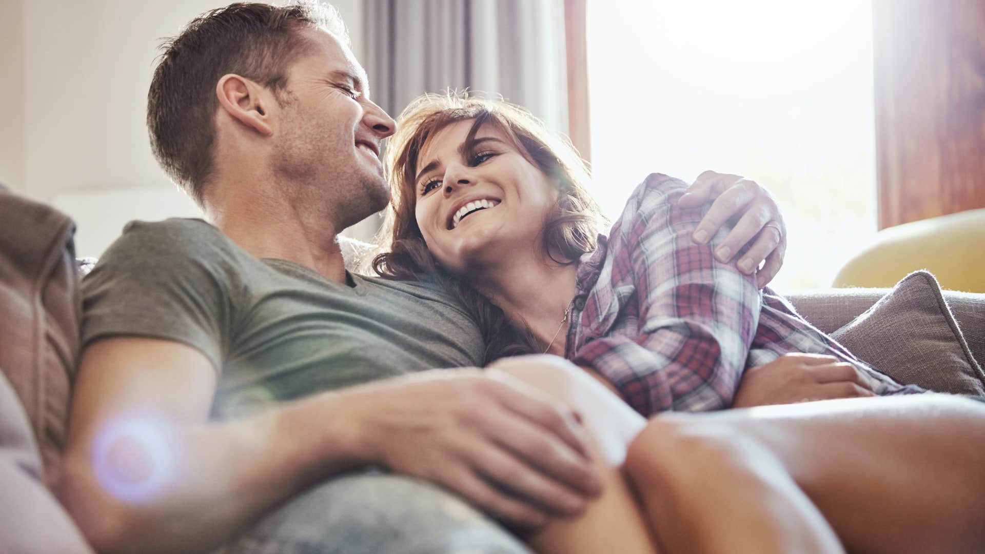 Man smiling and cuddling with his wife on the couch.