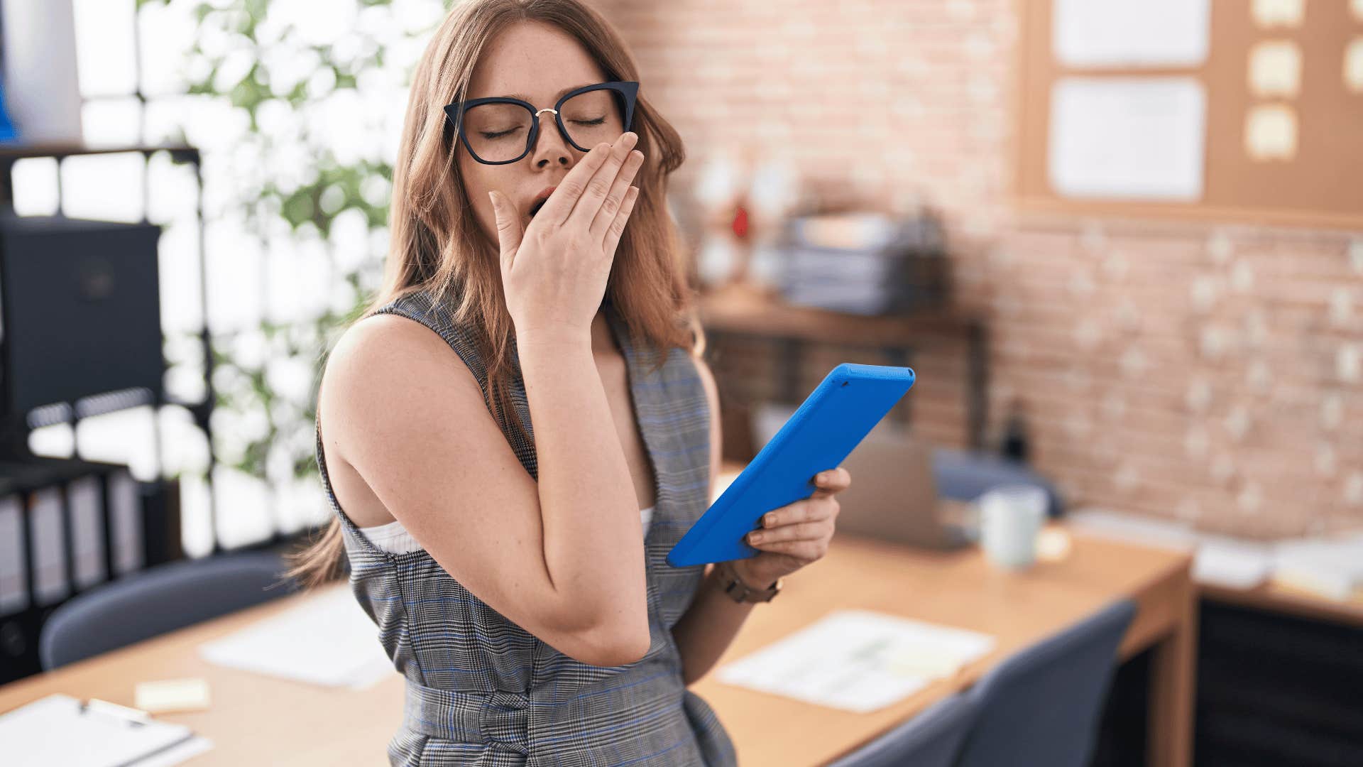 woman yawning while holding tablet