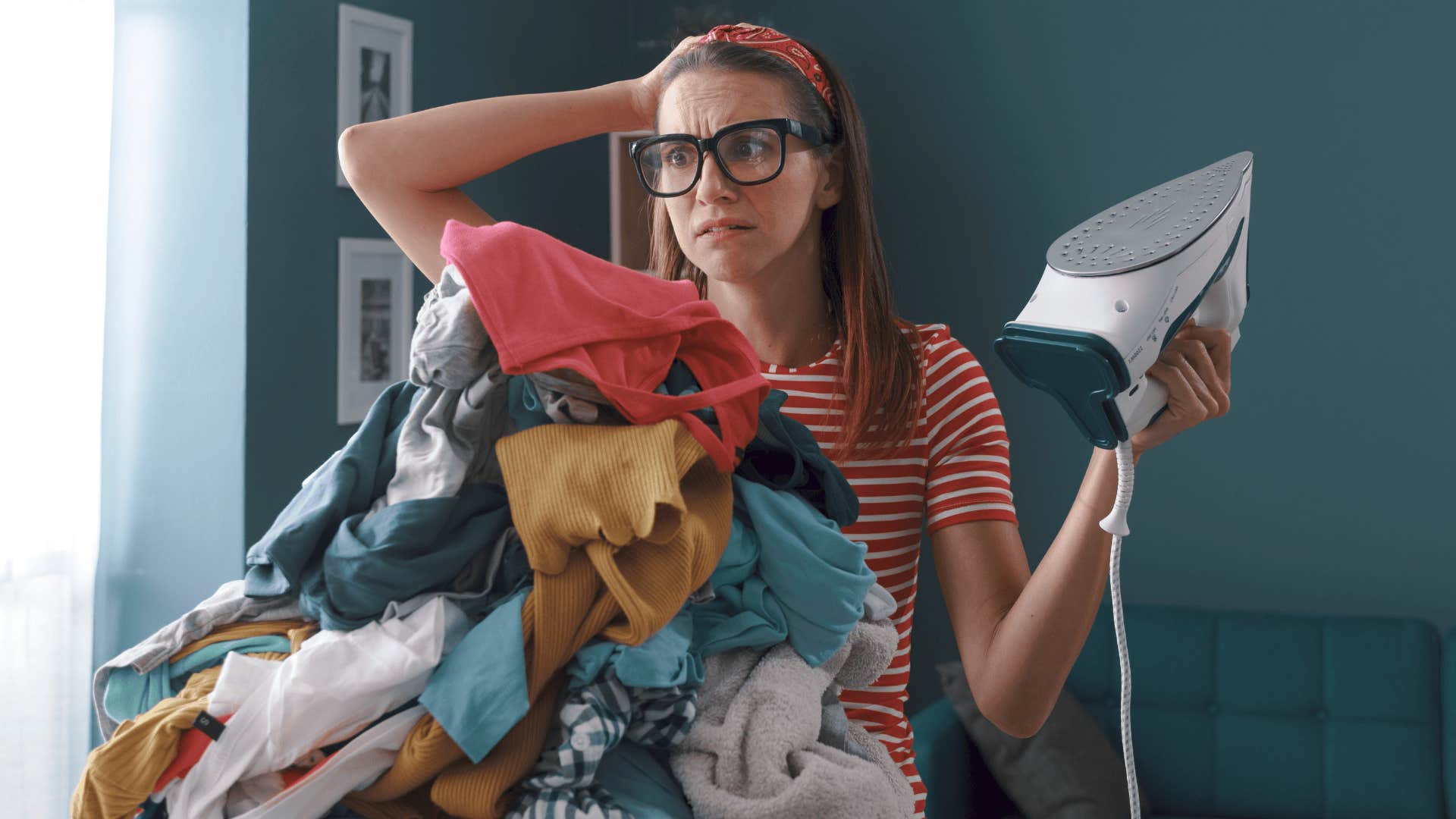 woman holding the iron and staring at a huge messy pile of clothes