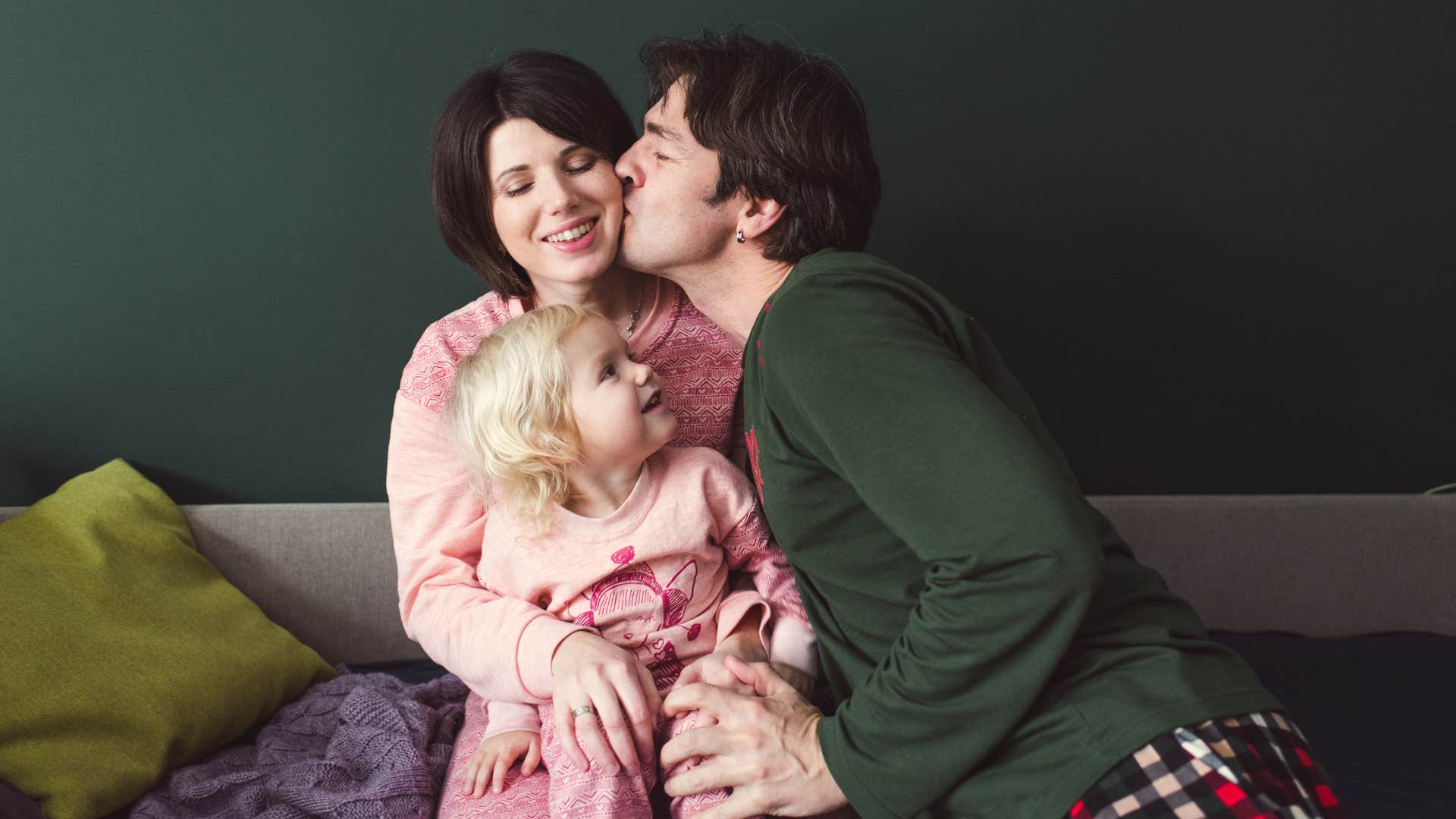 Mom and Dad embrace and kiss each other as the little daughter looks at them