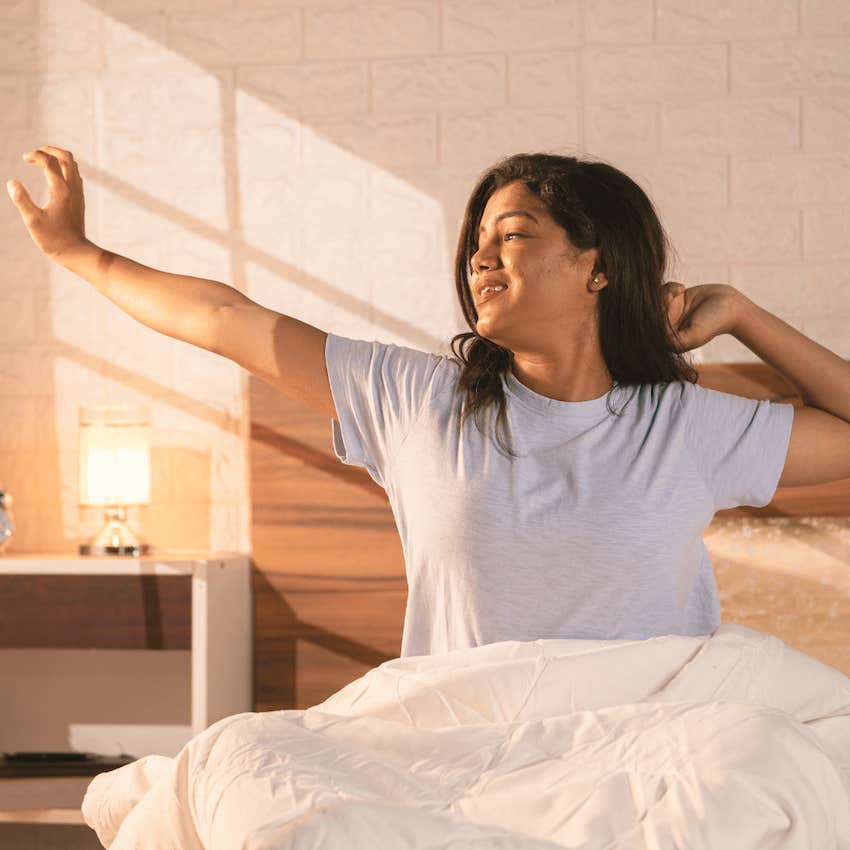 Woman stretches arms in bed after waking up