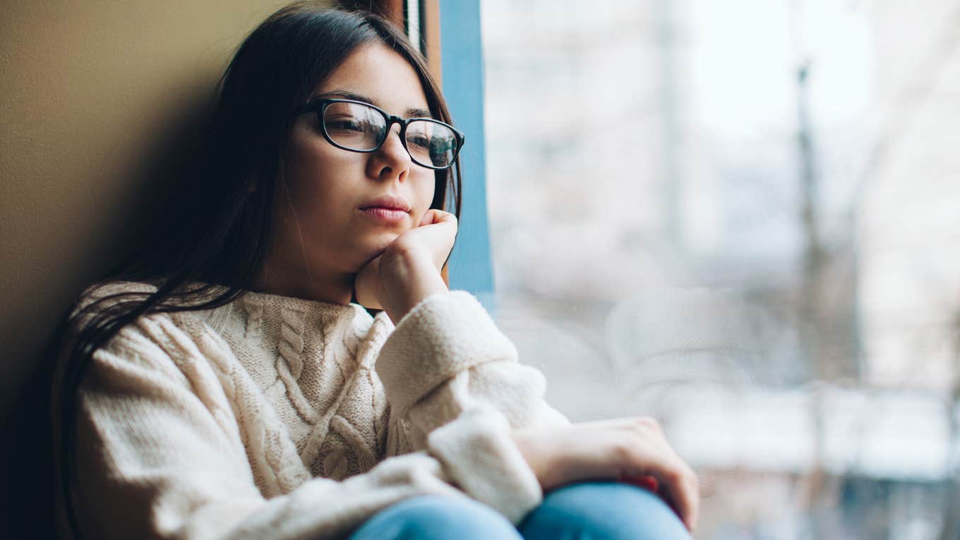 Sad young girl looking out a window.