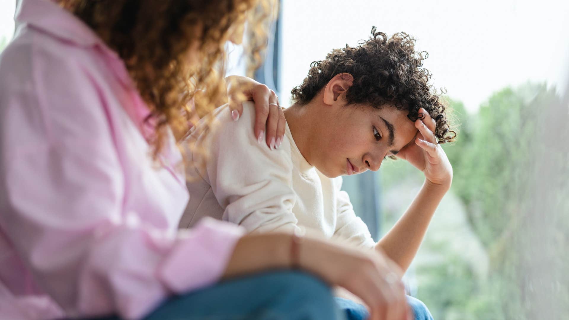 Young boy looking upset next to his mother