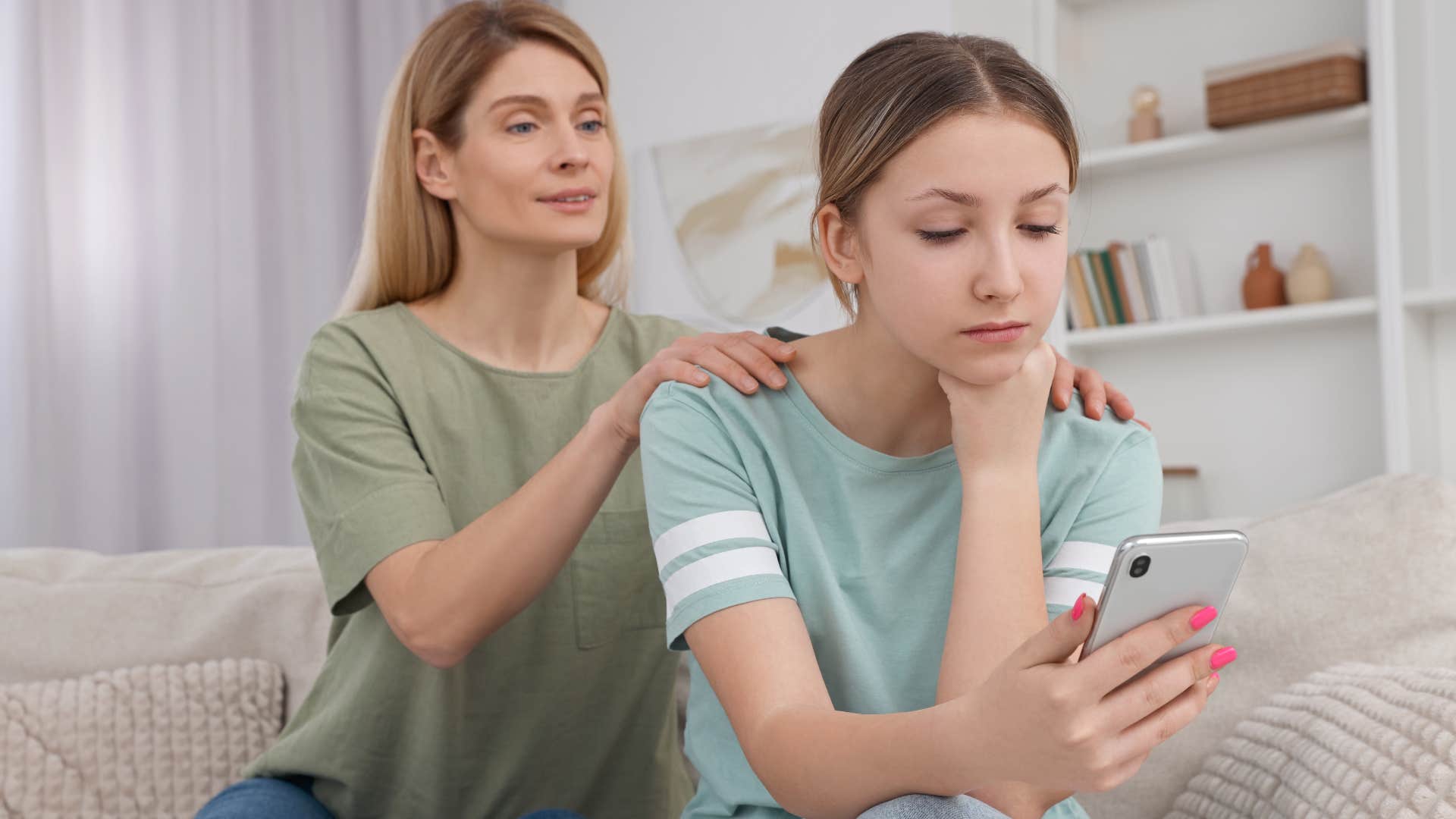 Woman comforting her upset daughter looking at her phone