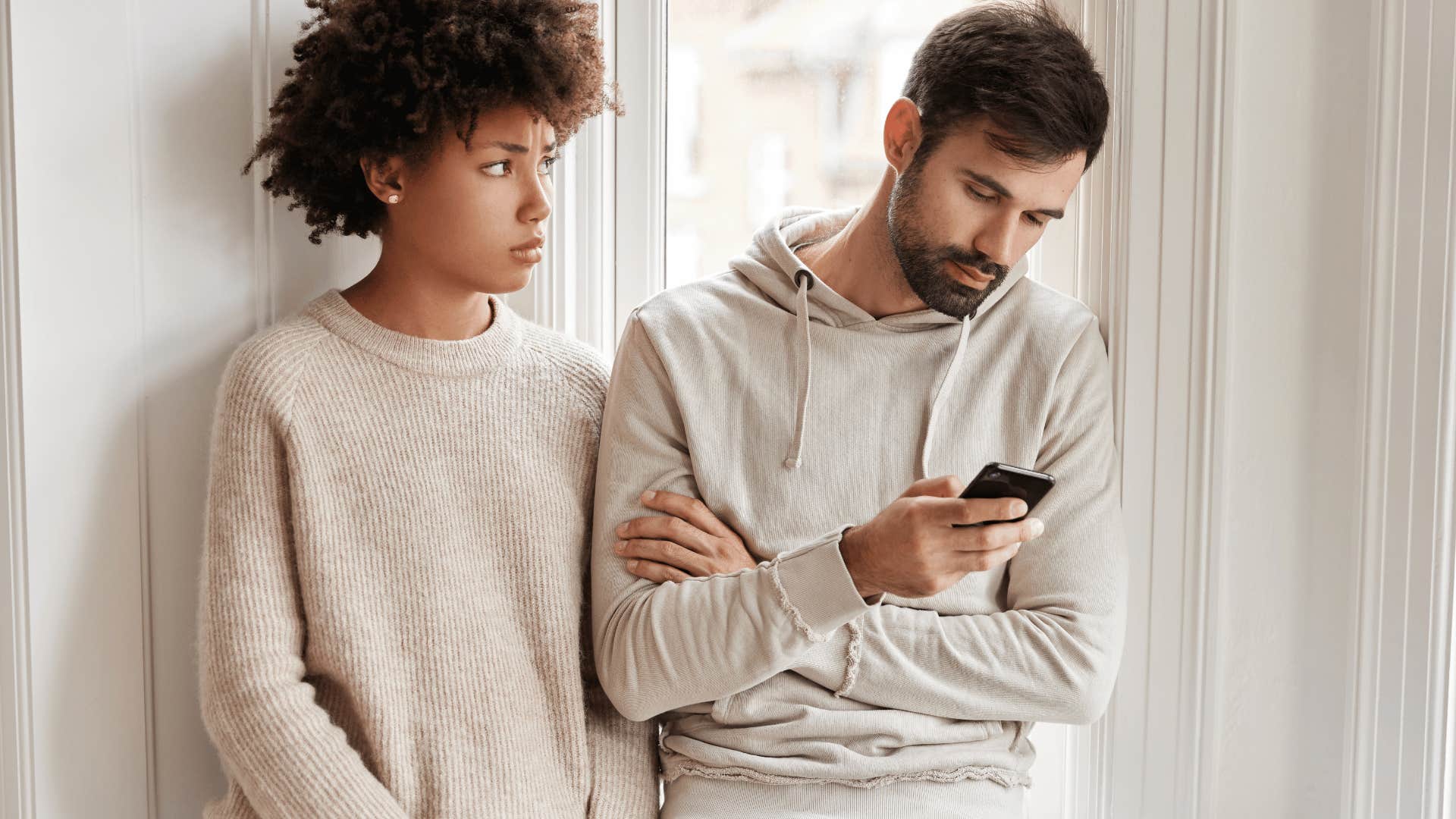 Unhappy woman looks at man who looks at his phone after making flimsy excuse 