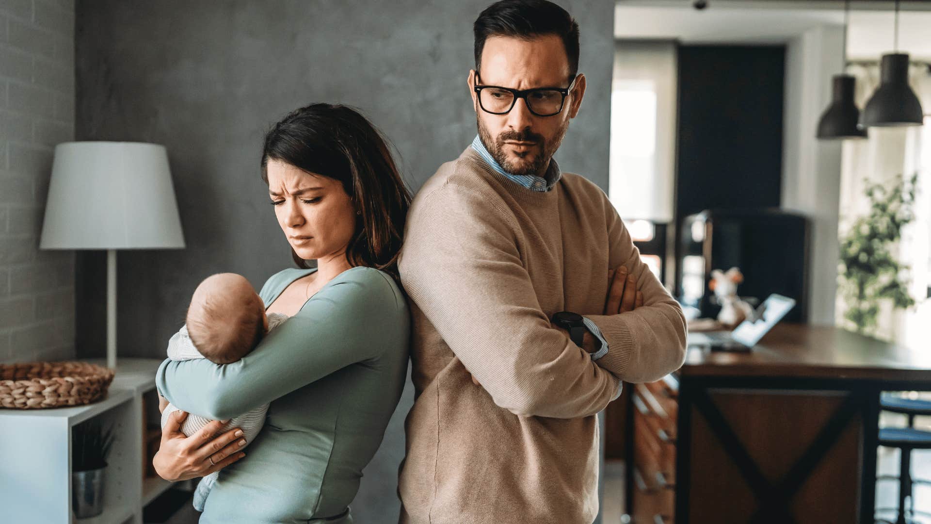 Woman holding babay stand back-to-back with passively aggressive man