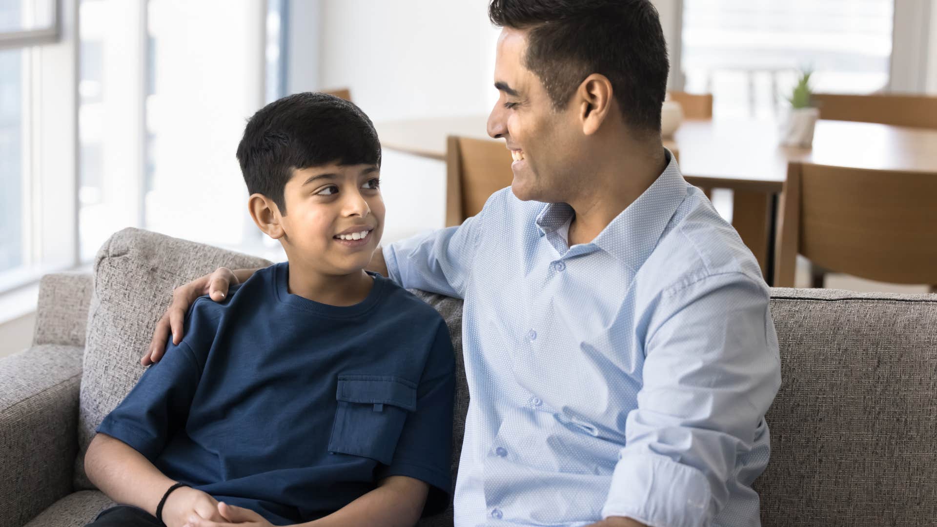 Dad comforting his smiling son on the couch.