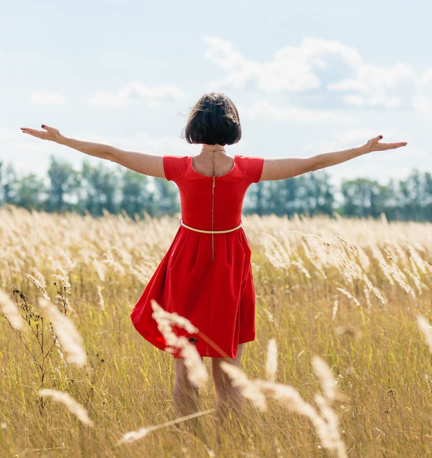 A woman stands with her back to the camera, arms outstretched in a gesture of freedom, amidst a golden wheat field