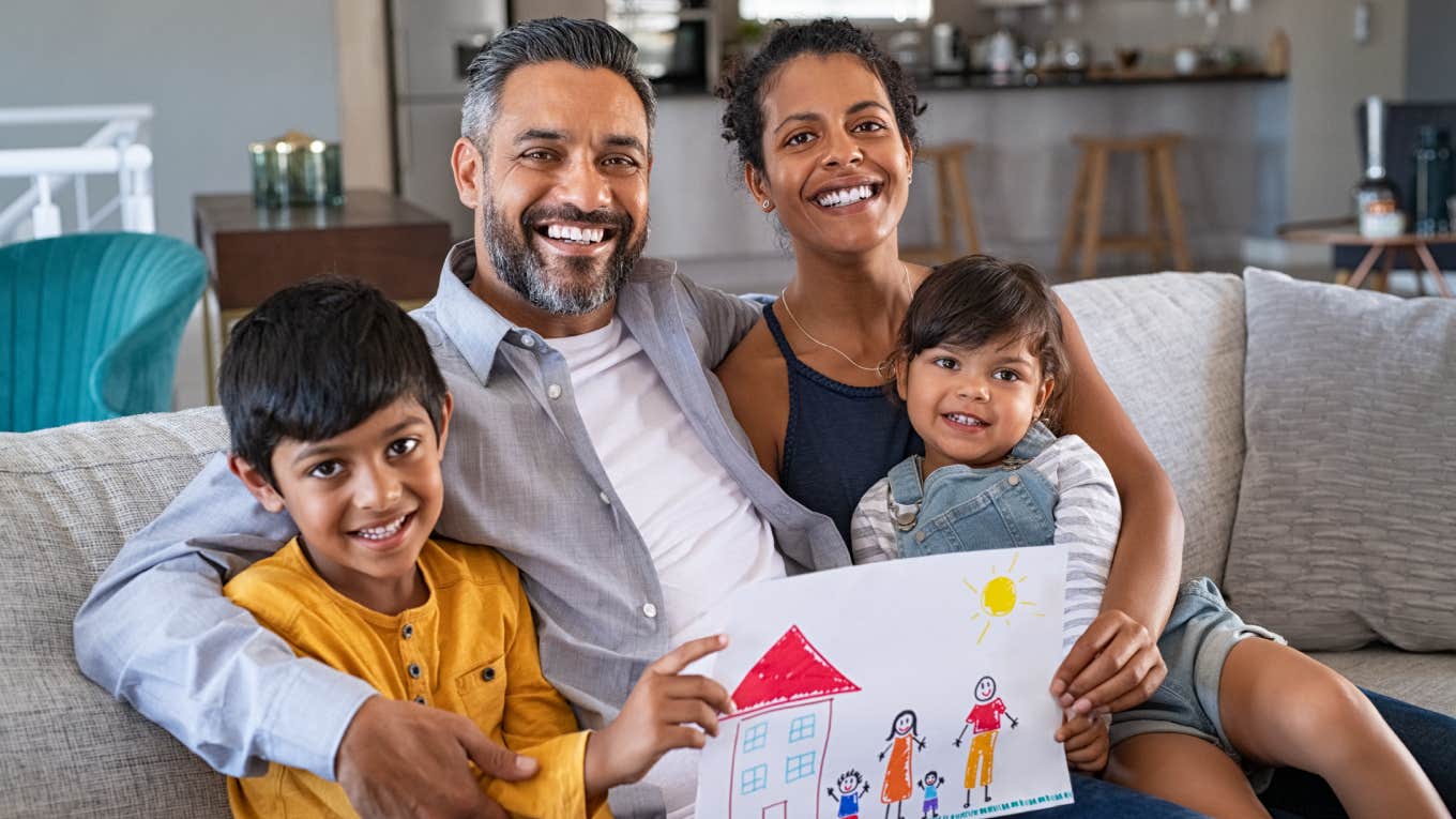 parents showing family painting of son and daughter sitting on sofa at home