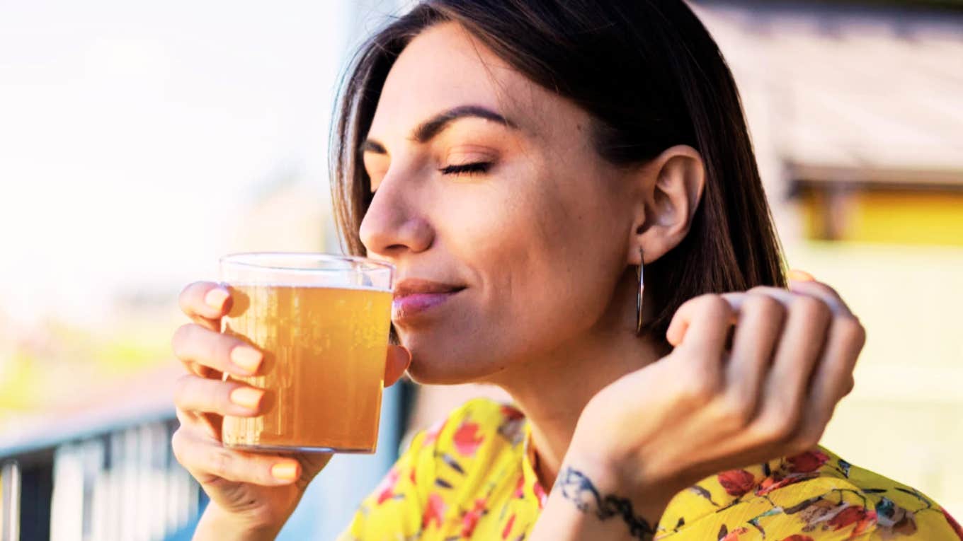 Woman smelling her cup of Kombucha, combatting hangover. 