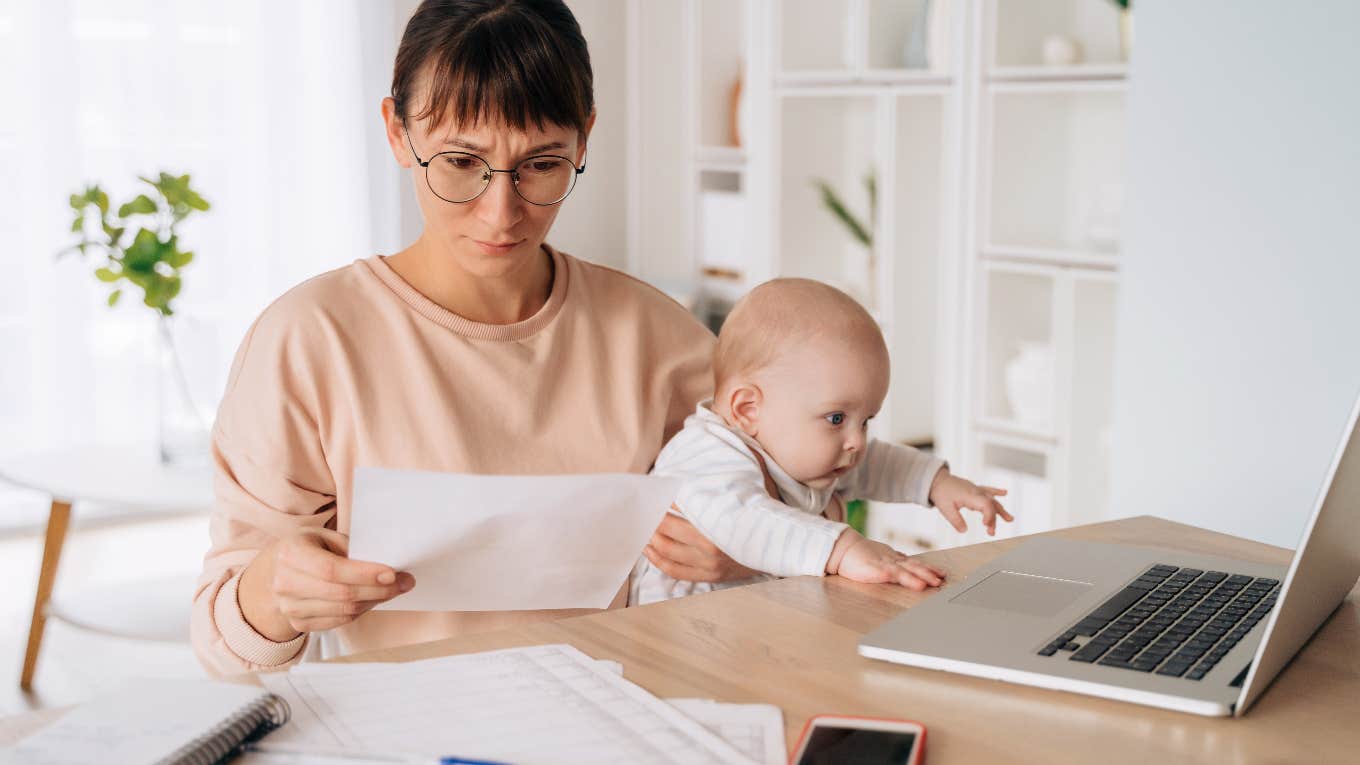 woman staring at bill in surprise while holding her baby