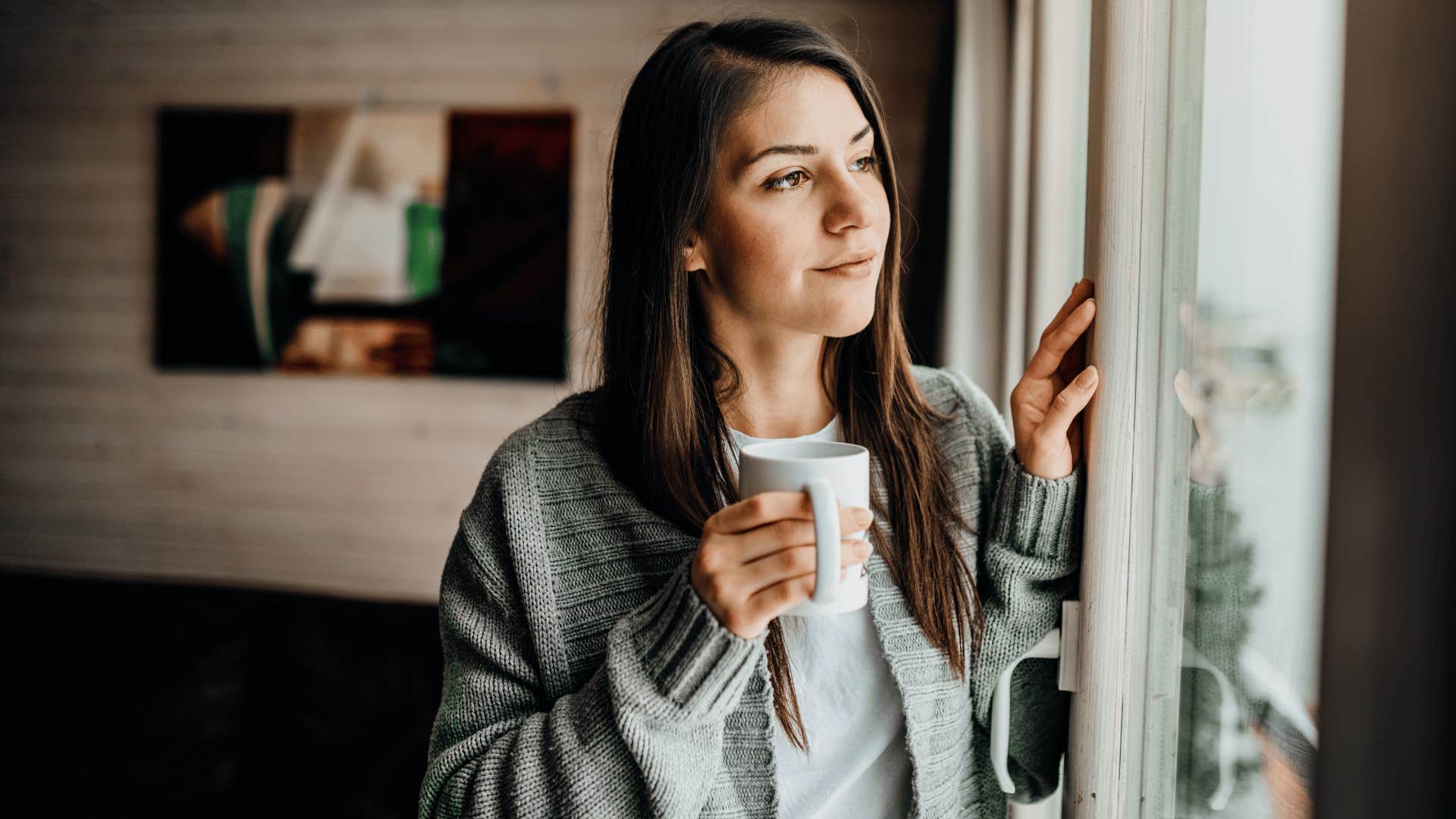 woman staring outside the window while drinking coffee