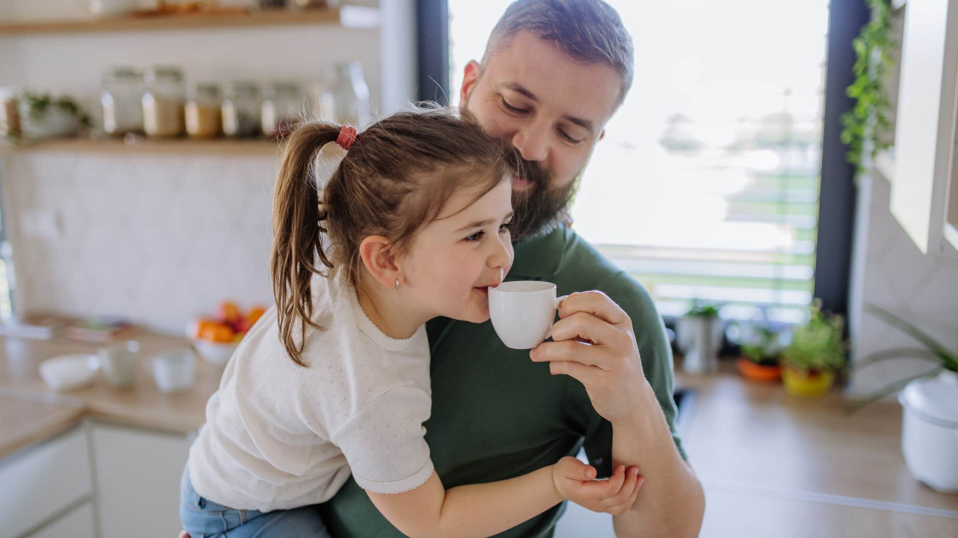 Father giving his little daughter cup with coffee to drink at home