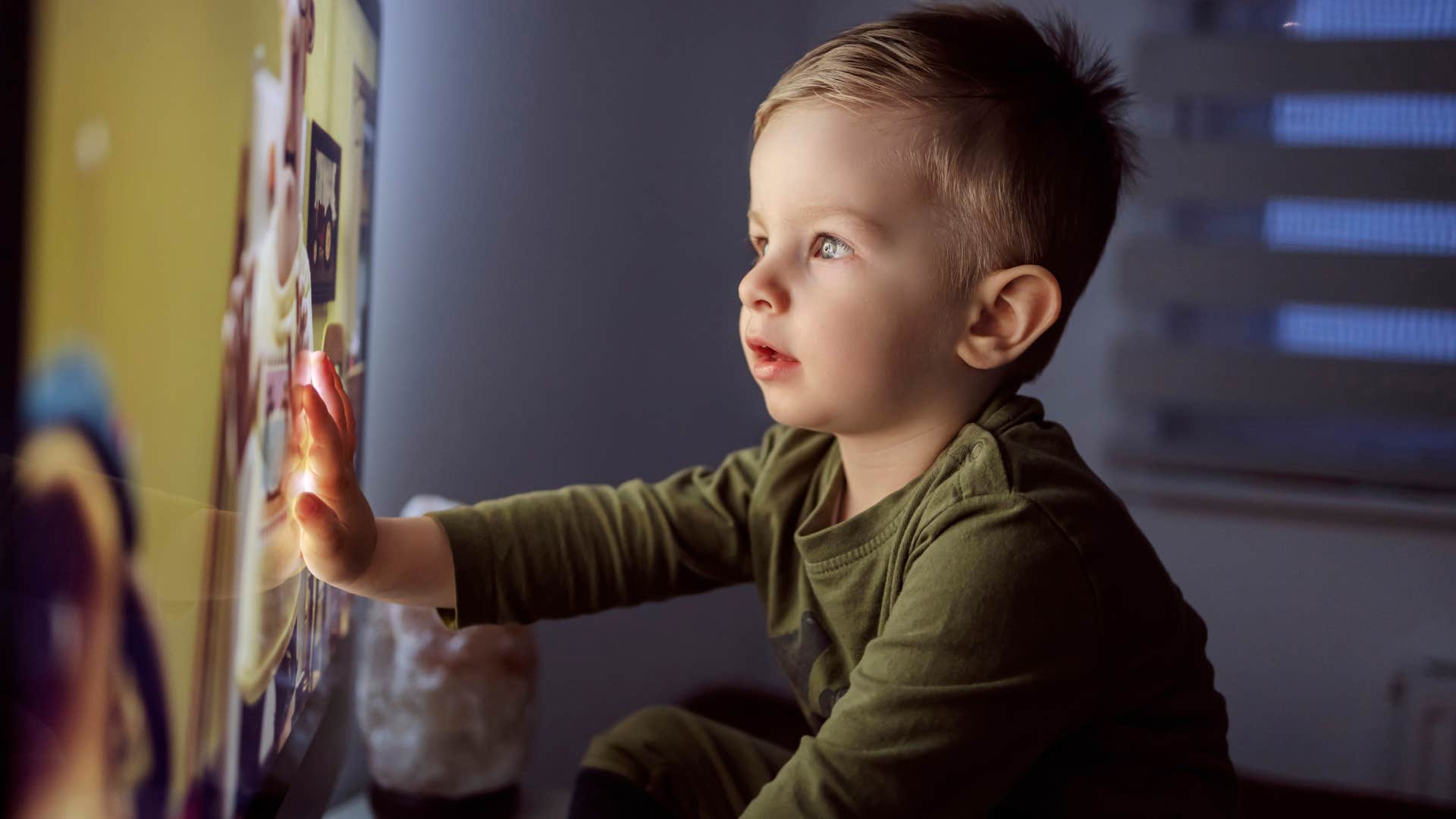 Close up of a kid sitting right in front of the TV in his pajamas and staring at a cartoon