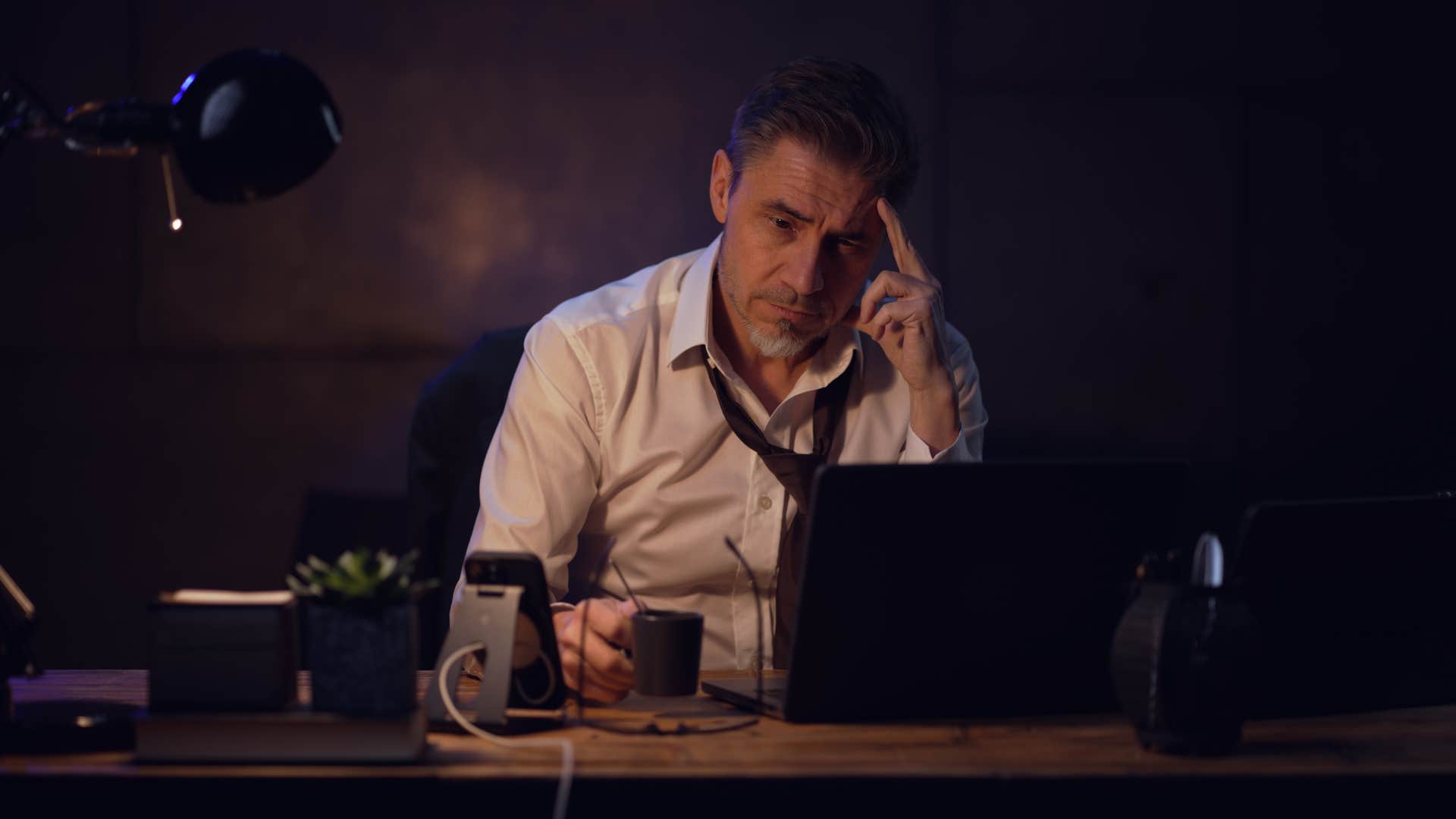 Businessman sitting at desk with laptop computer, working late in office, tired