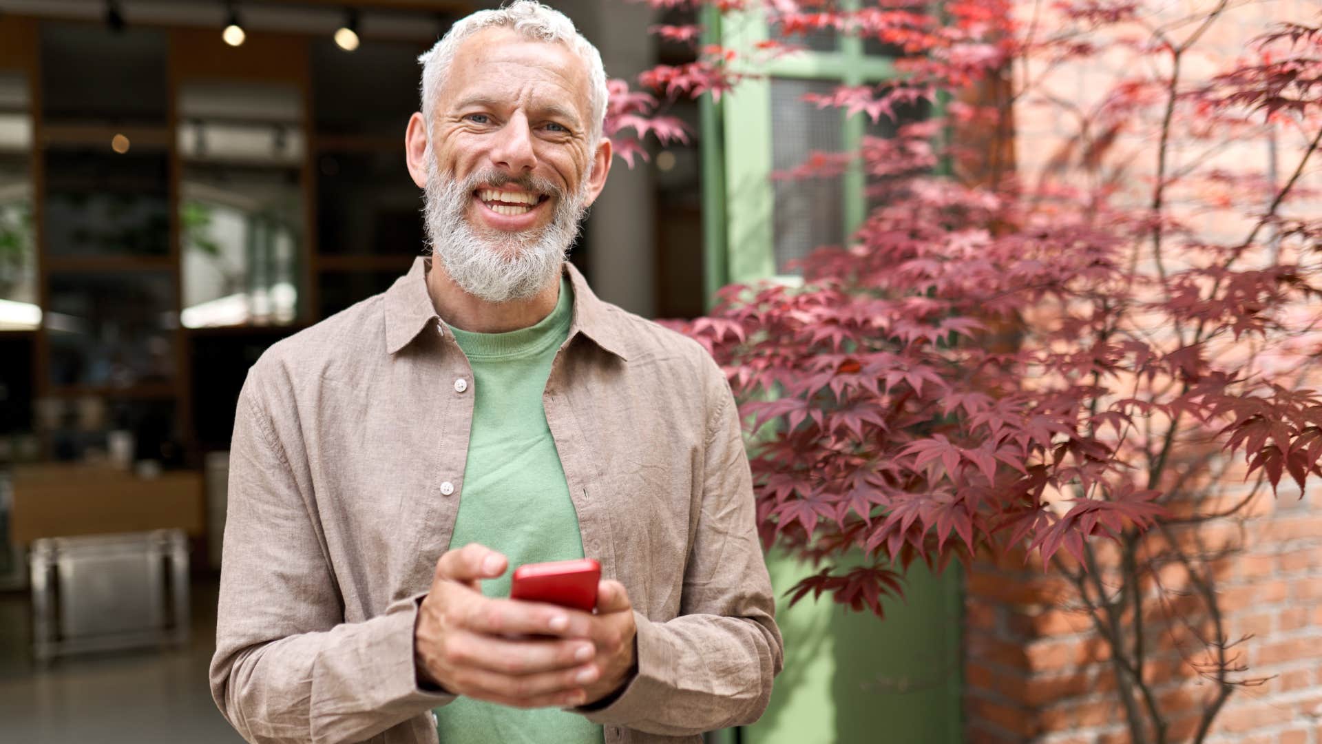 Smiling gray-haired older middle aged bearded man using mobile phone outdoors