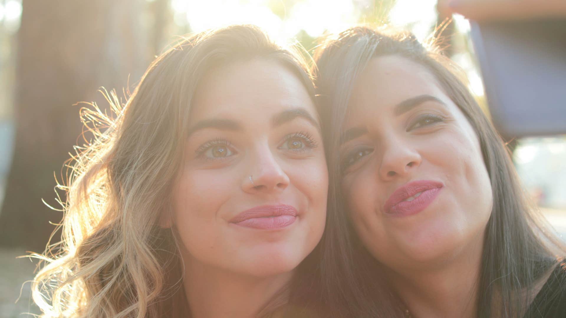 Two girlfriends holding cellphone posing for selfie